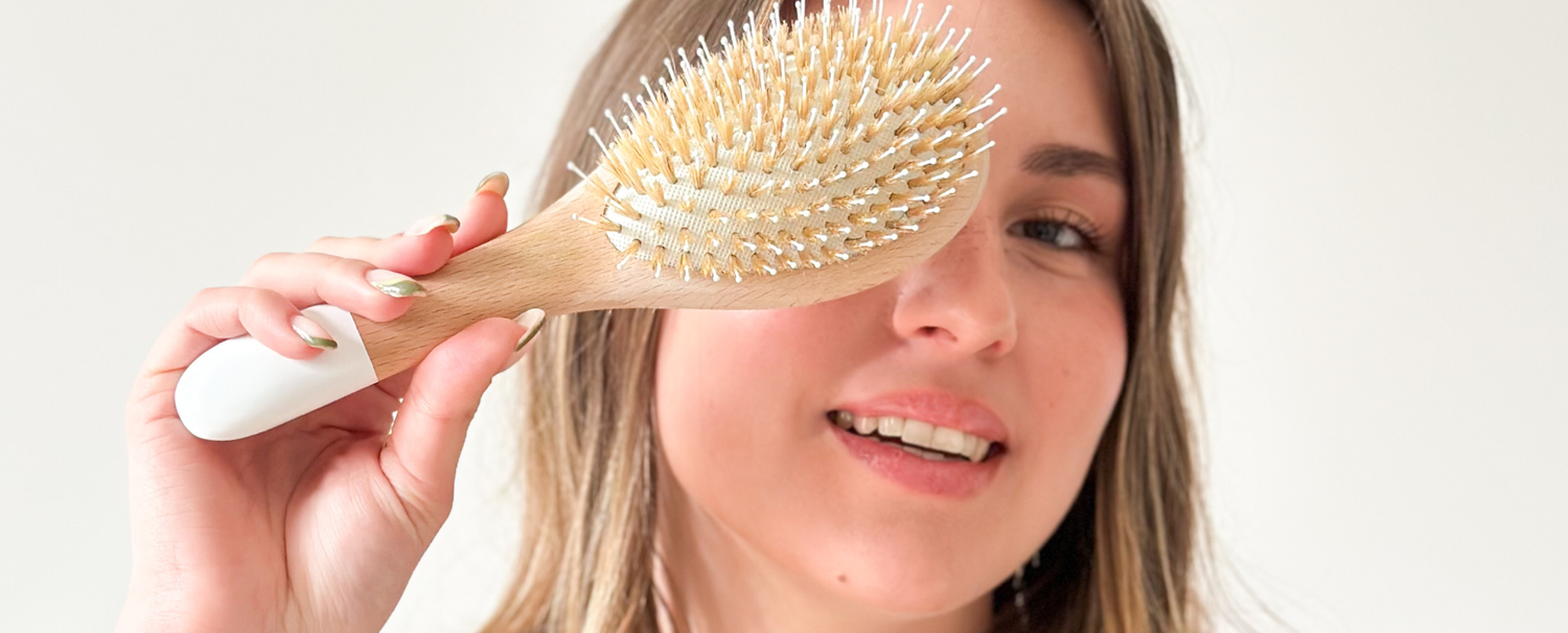 Jeune femme souriante portant dans sa main une brosse à cheveux démêlage et brillance de la marque Bachca.