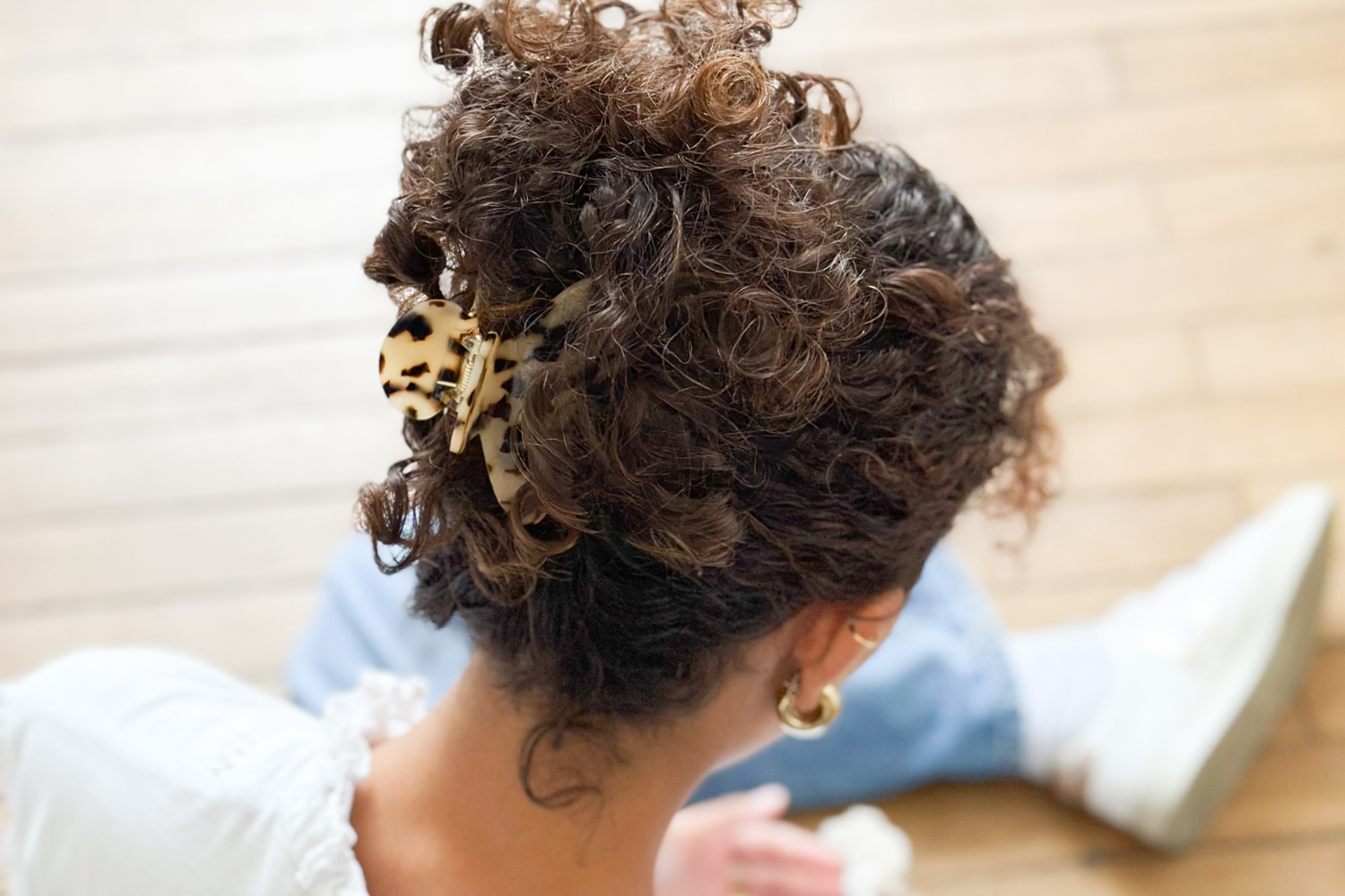 Femme aux cheveux bouclés assise de dos, gros plan sur ses cheveux attachés à l'aide d'une pince à cheveux écaille en grand format de la marque Bachca.