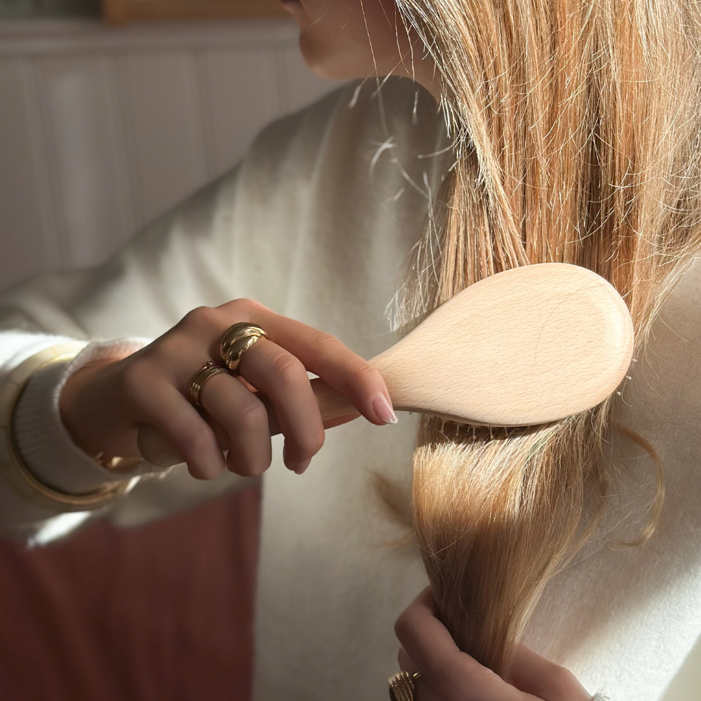 Photo lifestyle d'une femme blonde se brossant les cheveux avec la brosse soin et brillance de la marque Bachca.