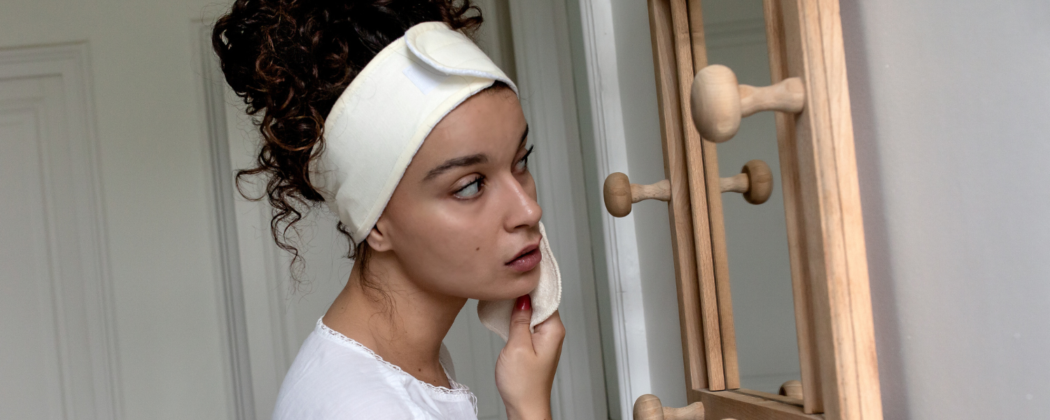 Femme qui porte un bandeaux soin Bachca qui se démaquille devant son miroir.
