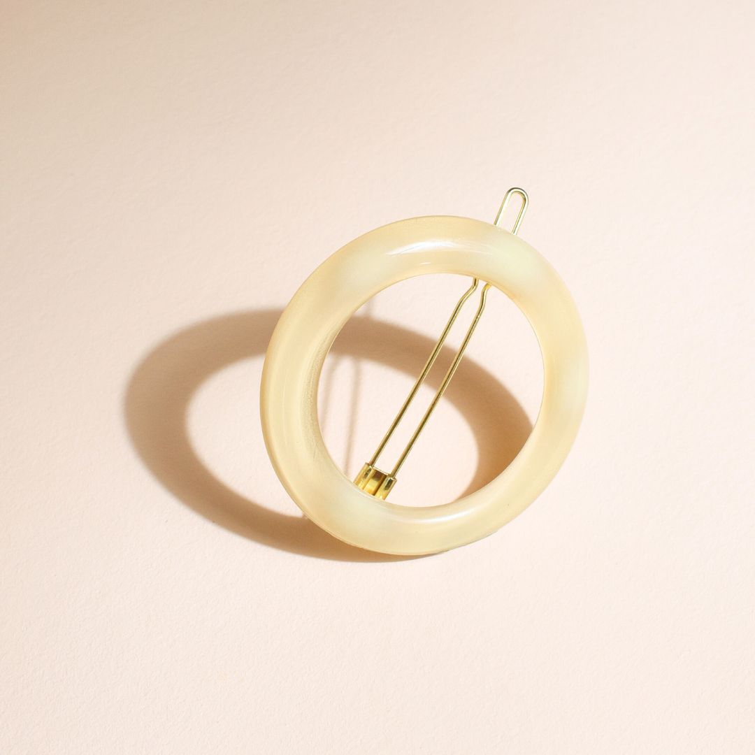 Barrette ronde ivoire Bachca posée sur fond nude, accessoire élégant pour sublimer les coiffures avec une touche minimaliste et raffinée.