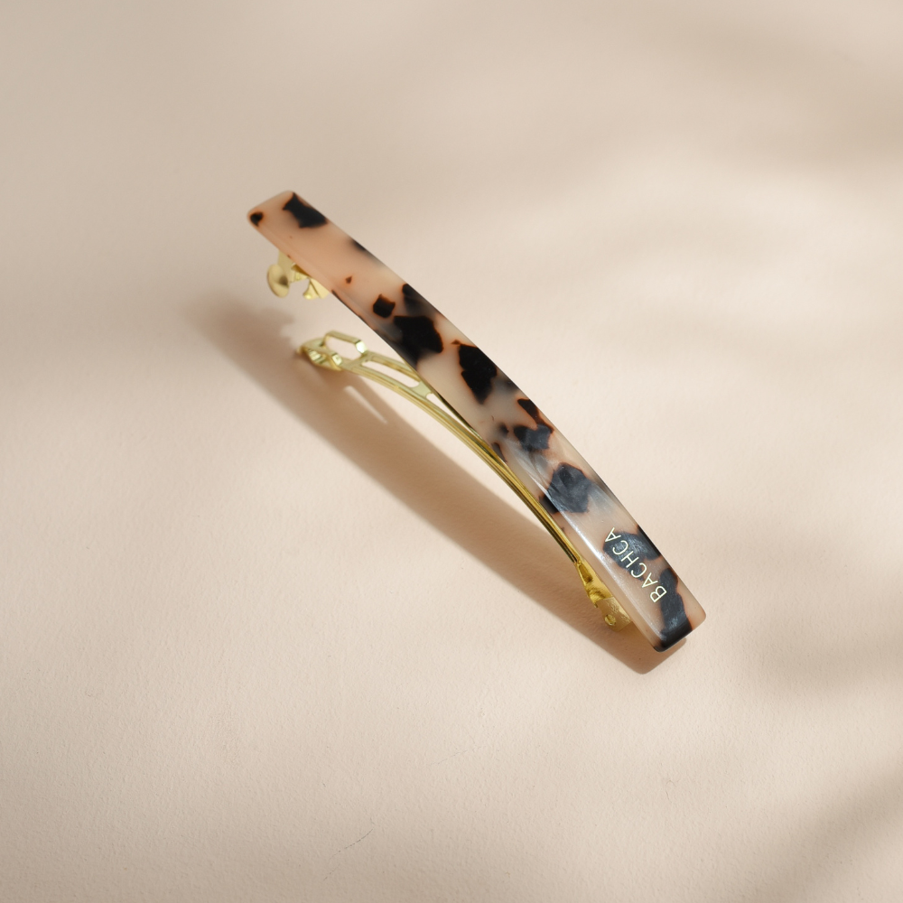 Barrette longue Bachca en acétate effet écaille, finition dorée et courbure élégante pour attacher les cheveux avec style.