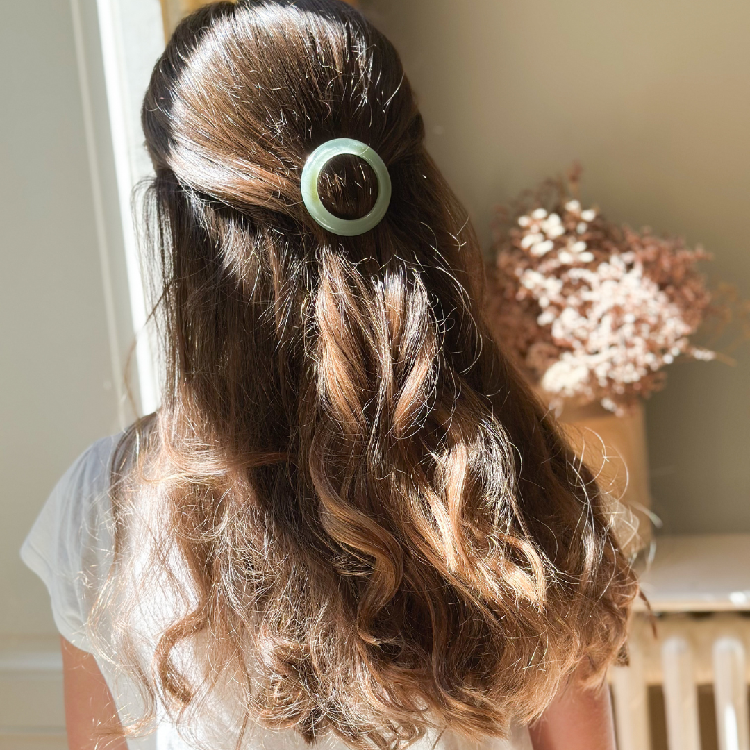 Chevelure bouclée attachée avec une barrette ronde couleur vert d'eau Bachca en acétate, portée dans un intérieur lumineux et naturel.