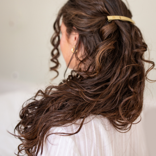 Femme aux cheveux bruns ondulés portant une barrette rectangulaire dorée Bachca, coiffure semi-attachée élégante et naturelle.