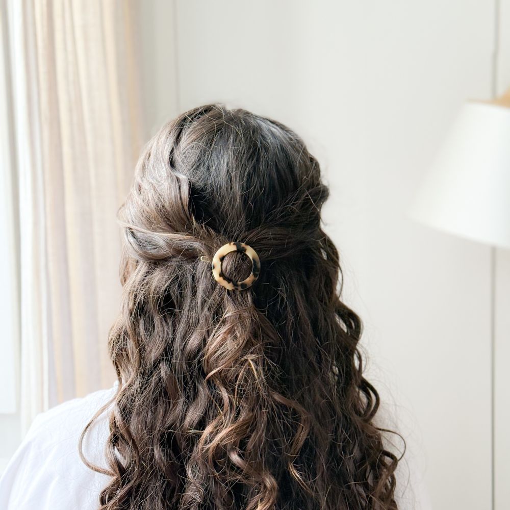 Femme aux cheveux bouclés portant une barrette ronde écaille Bachca pour attacher une demi-queue.