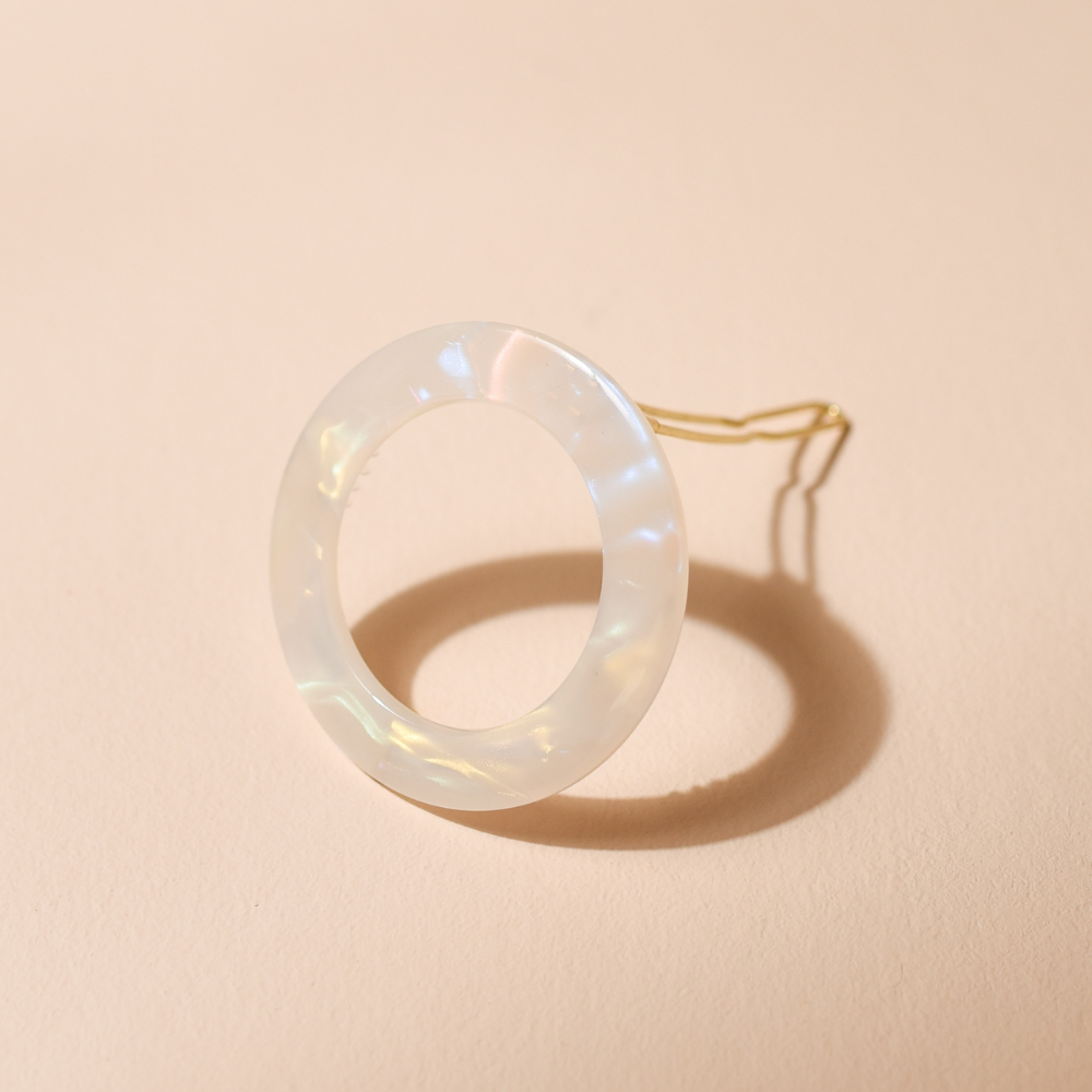 Barrette ronde nacrée Bachca posée debout sur fond beige, accessoire élégant en acétate.