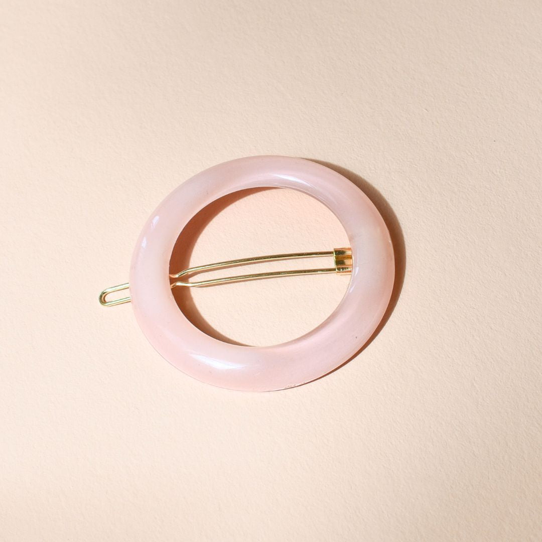 Barrette ronde rose dragée Bachca en acétate, posée à plat sur fond beige, avec monture dorée pour un style délicat et raffiné.