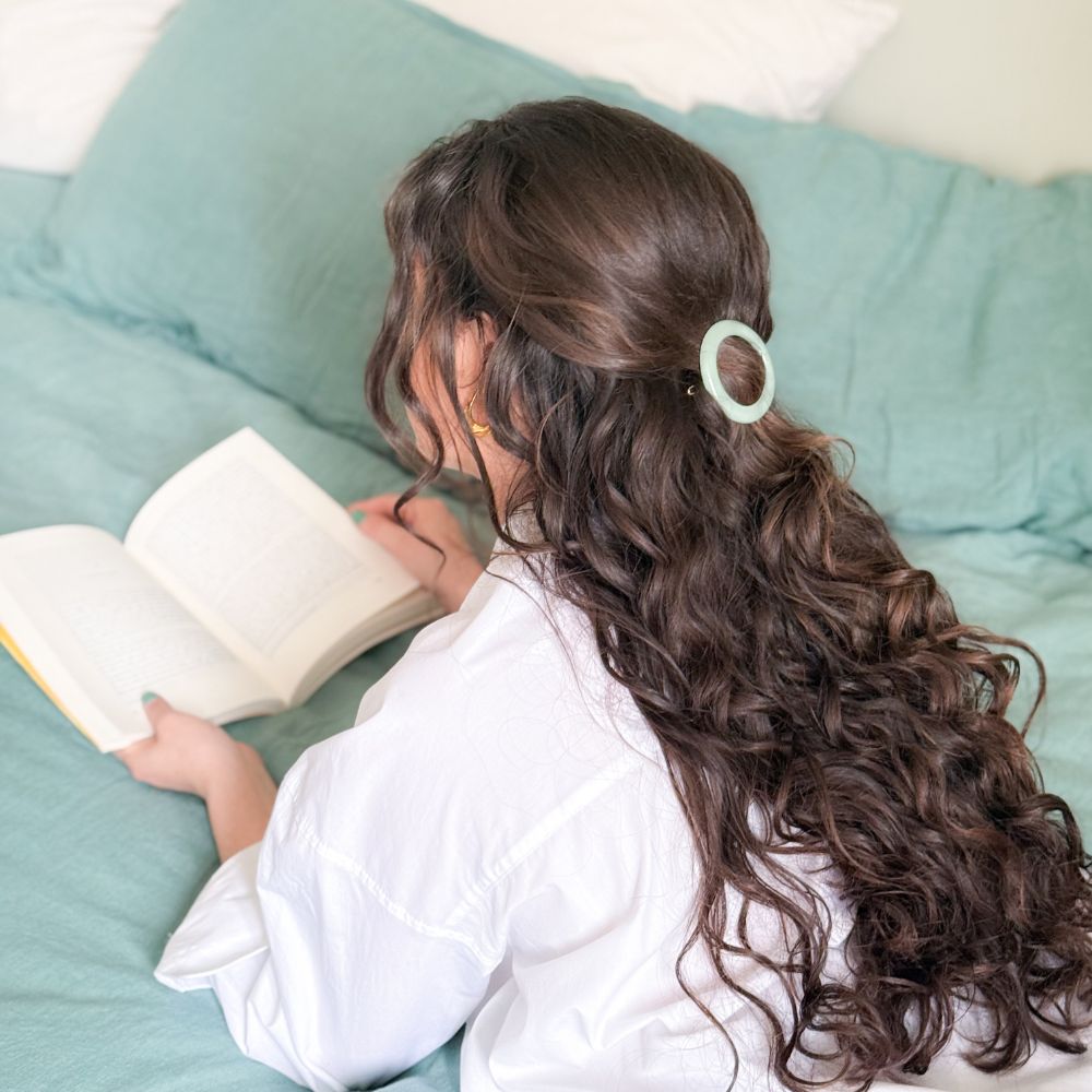 Femme aux cheveux bouclés allongée, coiffée d’une barrette ronde vert d’eau Bachca.