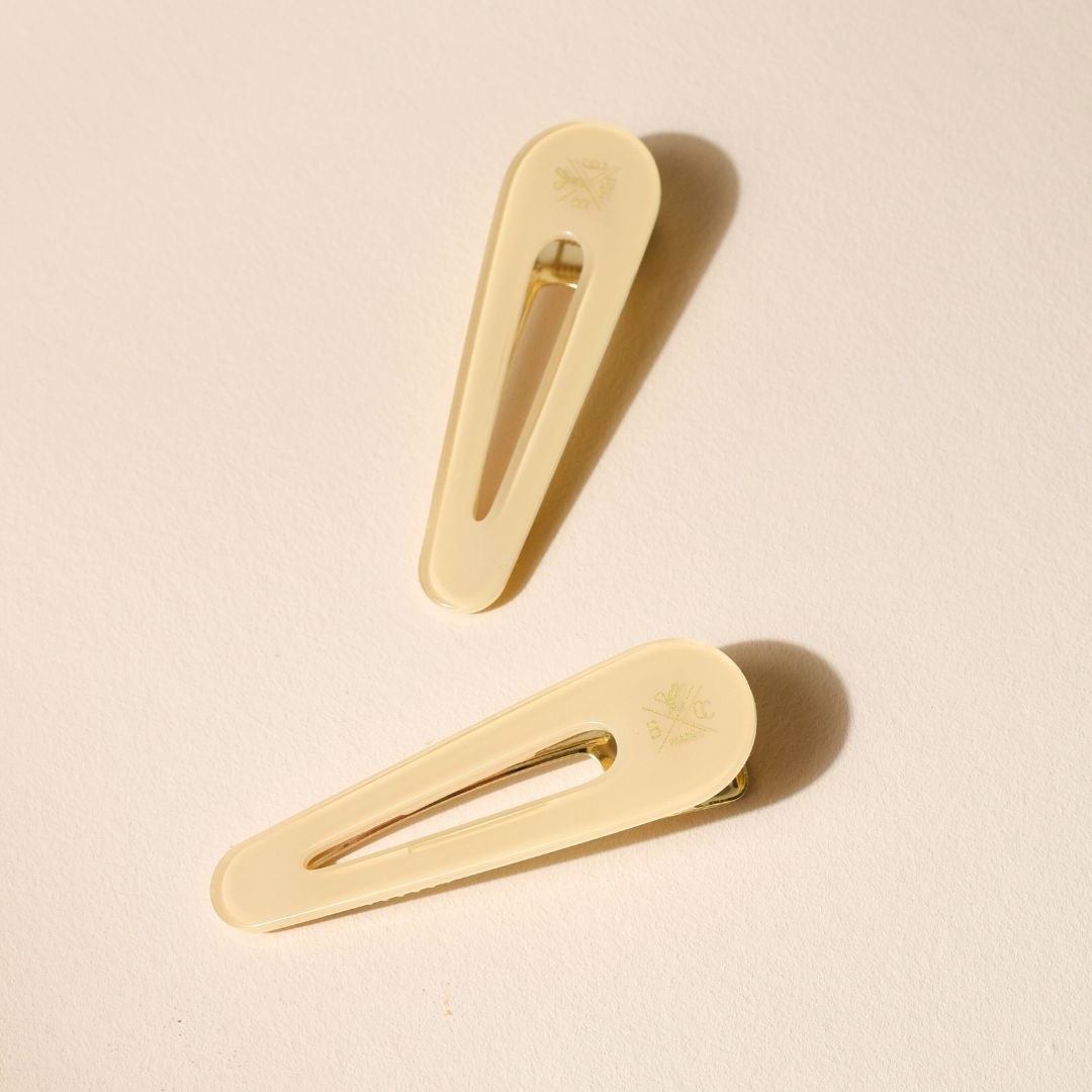 Lot de deux barrettes plates Bachca en acétate ivoire avec finition brillante et fermoir doré, posées sur fond beige.