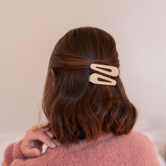 Cheveux bruns mi-longs attachés en demi-queue avec deux barrettes ivoire Bachca, coiffure élégante et tendance.