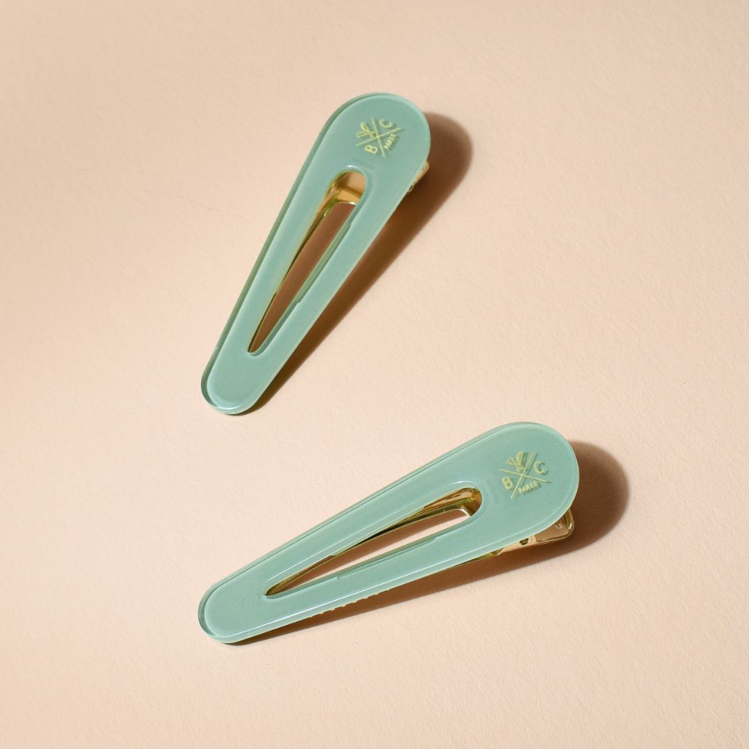 Lot de deux barrettes plates Bachca en acétate vert d’eau avec fermoir doré, élégantes et minimalistes, posées sur fond beige.