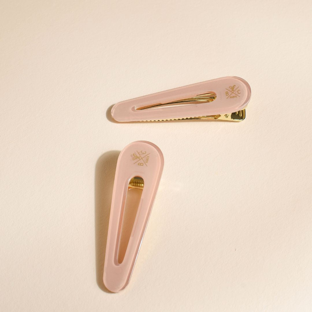 Lot de deux barrettes plates Bachca en acétate rose dragée avec fermoir doré, disposées à plat sur fond beige.