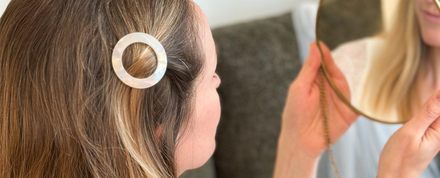 Gros plan sur une femme aux cheveux blonds portant une barrette ronde nacrée de la marque Bachca dans les cheveux.