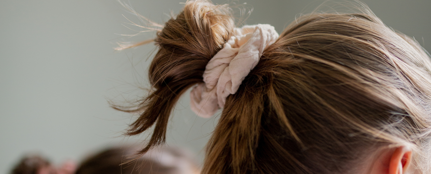 Gros plan sur les cheveux d'une jeune fille blonde attachés à l'aide d'un chouchou rose pâle de la marque Bachca.