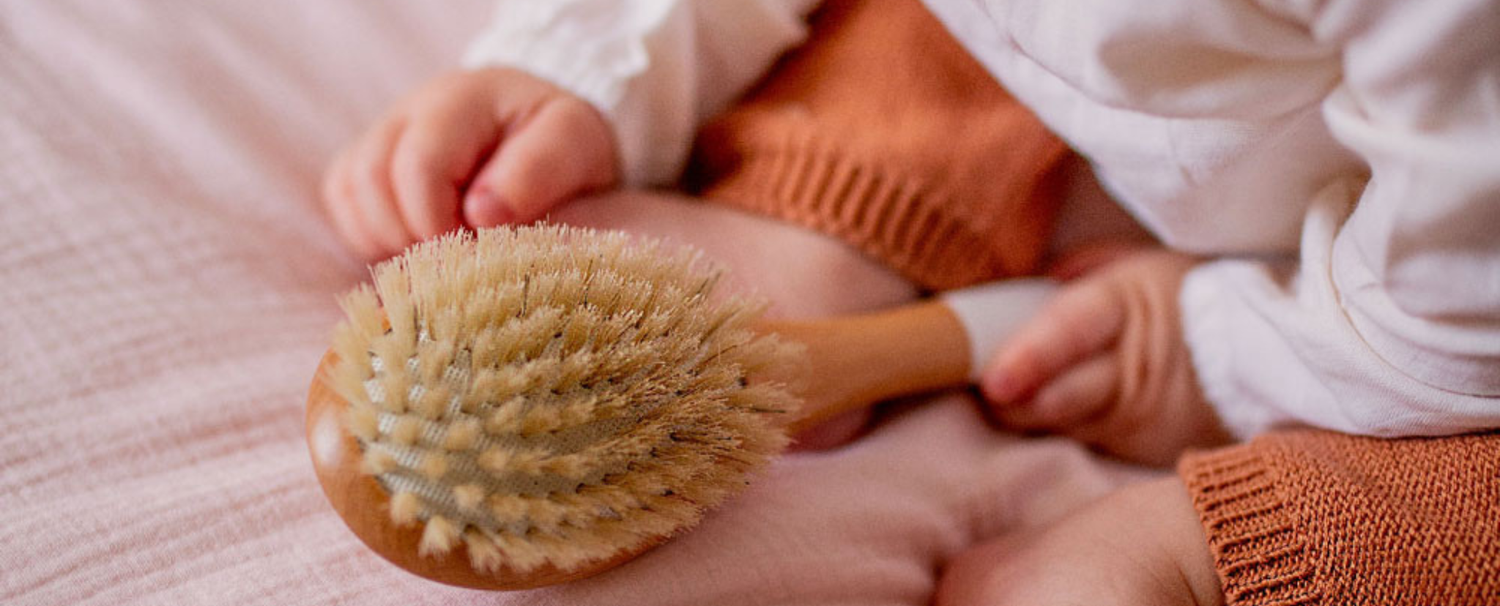 Mains de bébé tenant une brosse à cheveux en poils 100% sanglier de la marque Bachca.