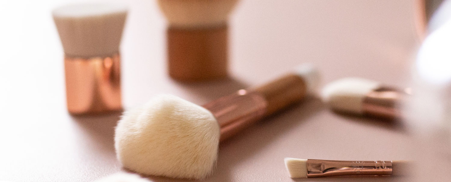 Différents pinceaux à maquillage de la marque Bachca disposés sur une table rose.