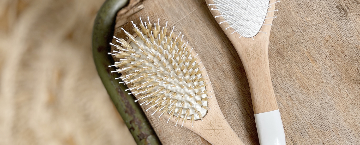 Deux brosses à cheveux de la marque Bachca posées sur un tabouret en bois.