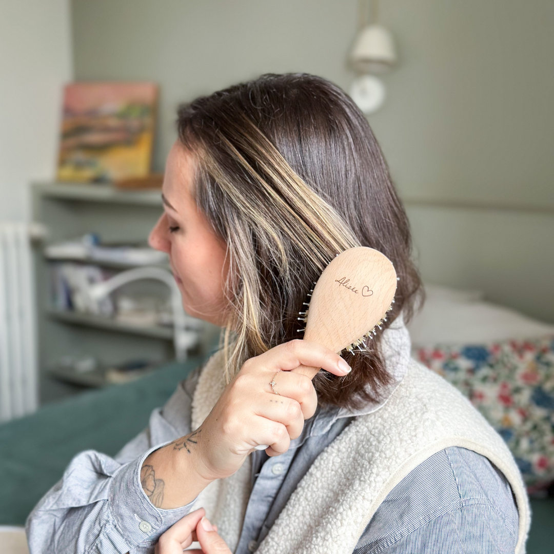 Femme souriante se brossant les cheveux avec une brosse Bachca en bois gravée "Alizée ❤️".