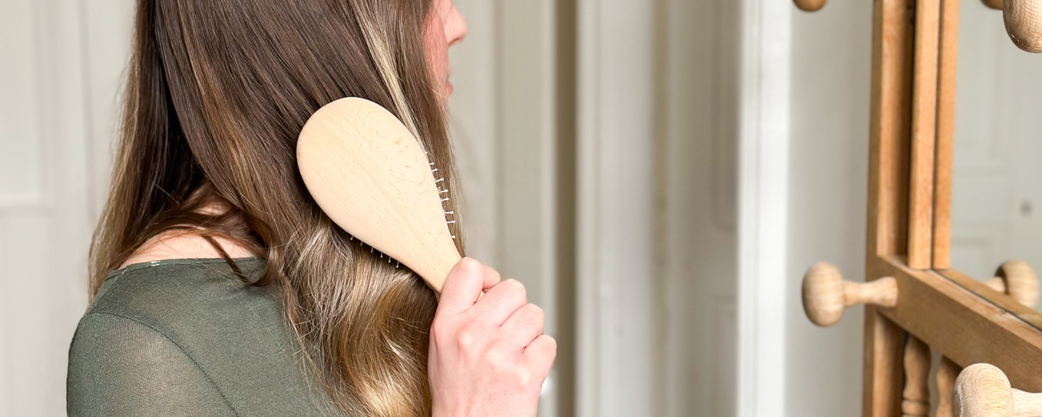 Femme qui se brosse les cheveux devant le miroir à l'aide d'une brosse à cheveux de la marque Bachca.