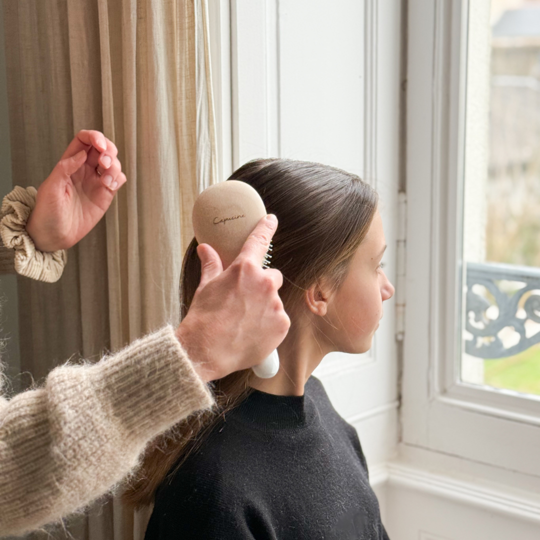 Brossage des cheveux dâune jeune fille avec une brosse personnalisĂ©e Bachca prĂšs dâune fenĂȘtre.