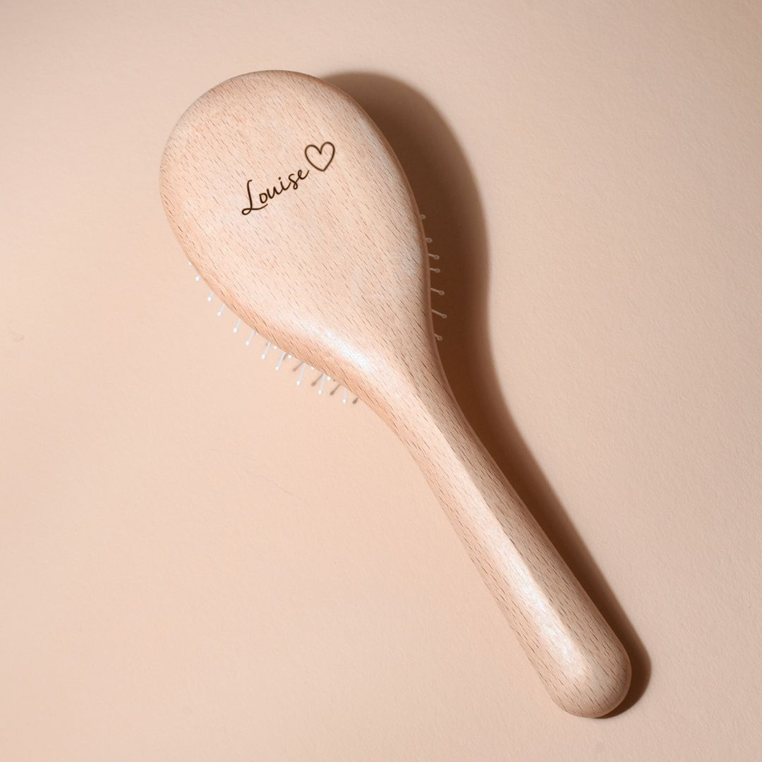 Brosse à cheveux Bachca en bois de hêtre clair, personnalisée avec le prénom « Louise » suivi d’un petit cœur gravé sur le dos, posée sur un fond beige doux.