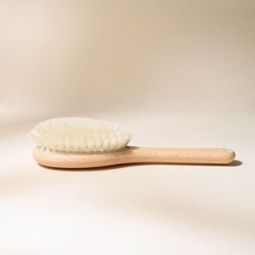 Brosse à cheveux pour bébé Bachca posée sur fond beige, en bois de hêtre naturel avec poils ultra doux, photographiée en gros plan de profil.