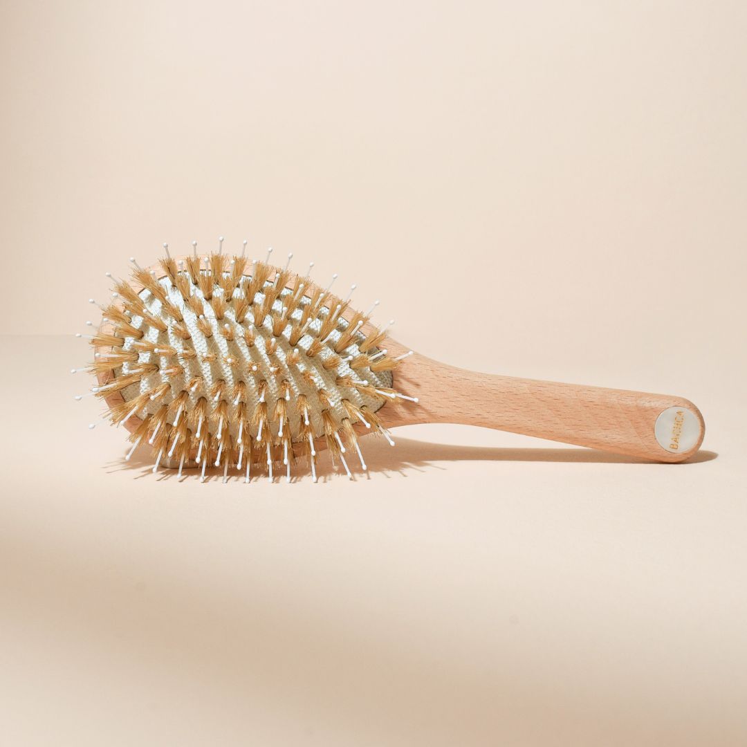 Brosse à cheveux petit format Bachca vue du dessus, montrant les picots en sanglier et nylon, manche en bois de hêtre avec pastille nacrée, posée sur fond beige uni.