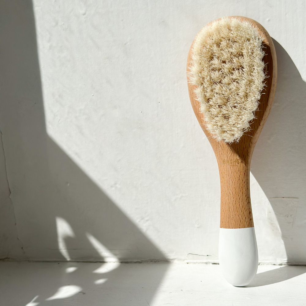 Brosse bébé Bachca en poils de chèvre posée verticalement sur un rebord de fenêtre blanc.