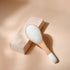 Brosse Bachca démêlage et volume en bois de hêtre et manche blanc, posée sur son étui rose poudré.