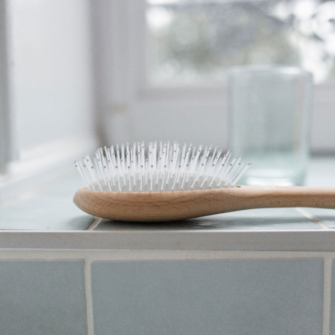 Brosse démêlage et volume Bachca aux picots souples et en bois naturel, posée sur le rebord d'une baignoire blanche, dans une ambiance douce et épurée.