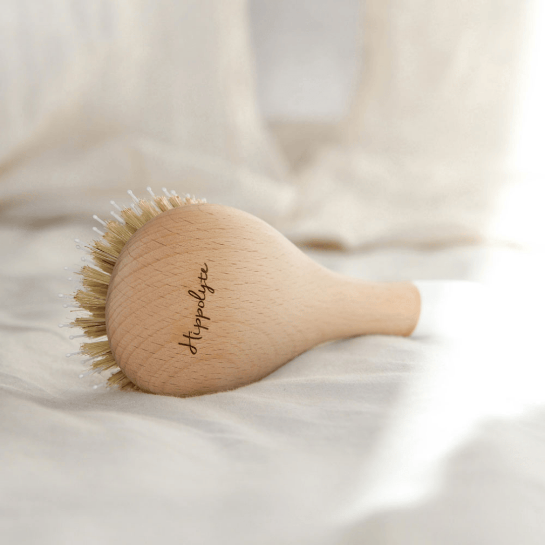 Brosse à cheveux Bachca en bois de hêtre brut personnalisée avec le prénom Hippolyte, posée sur du linge blanc.