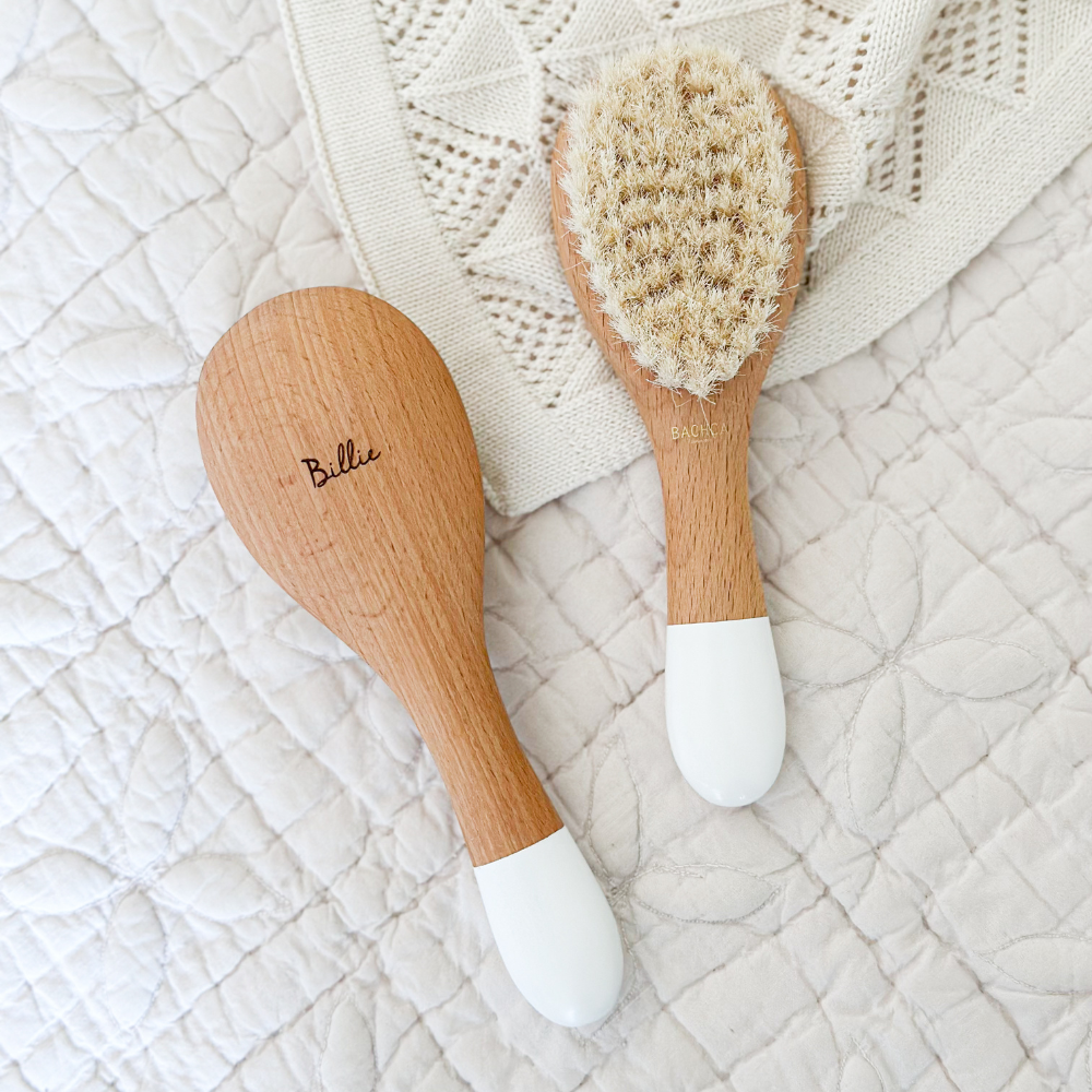 Deux brosses à cheveux de la marque Bachca sur une couette texturée beige. Une des deux brosses est gravée avec le prénom Billie.
