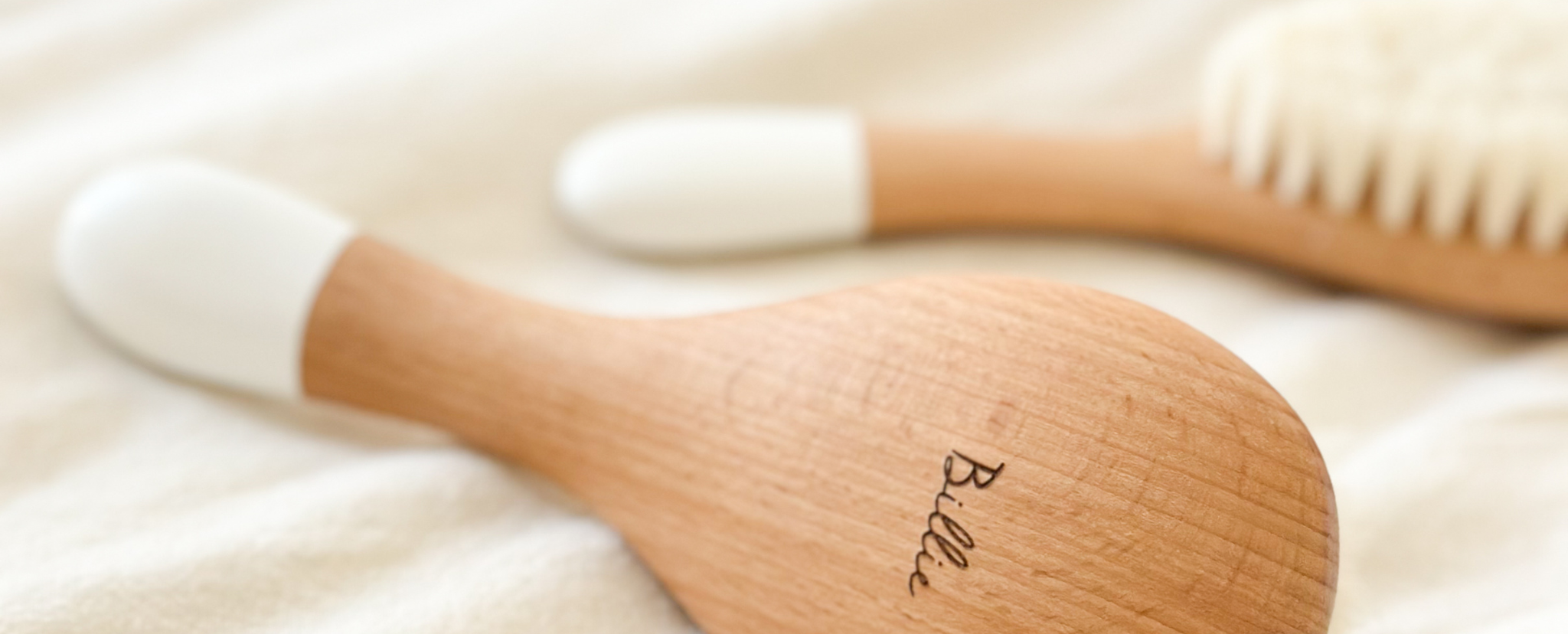 Gros plan sur une brosse nourrisson gravée au nom de Billie sur une brosse en bois, couleurs chaudes et douces.