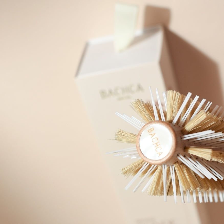 Gros plan sur la tête de la brosse ronde brushing Bachca vue de face, avec poils en nylon et soie de sanglier, positionnée devant son étui beige portant le logo de la marque.
