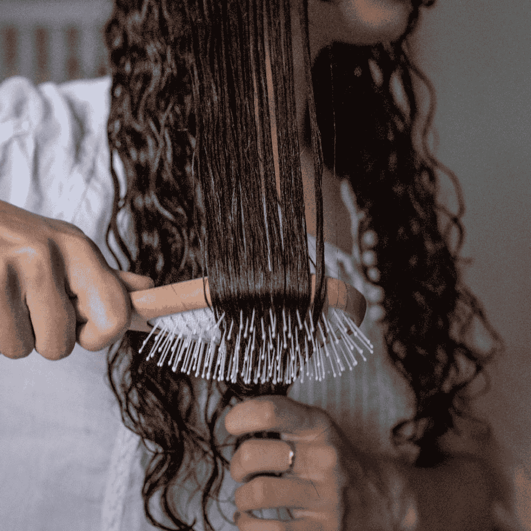 Femme démêlant ses cheveux mouillés et bouclés avec une brosse démêlante Bachca à picots souples, en bois naturel.