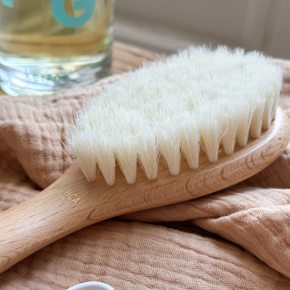 Brosse bébé naissance en soie de chèvre posée sur un linge de couleur terracota, zoom sur ses poils en soie de chèvre.