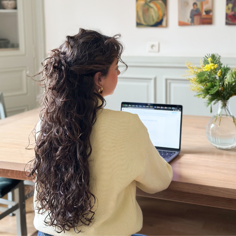 Femme de dos aux cheveux longs bouclés avec les cheveux attachés en chignon en demi-queue.