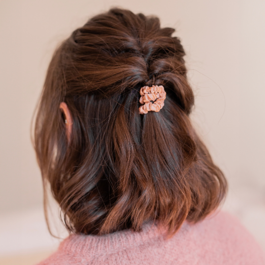 Coiffure demi-queue tressée sur cheveux courts avec un chouchou en soie rose Bachca, apportant une touche élégante et douce à un look décontracté.
