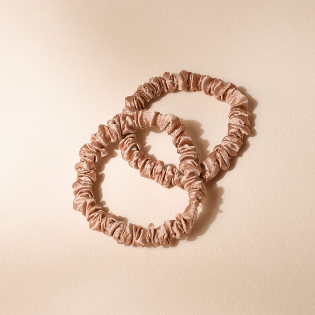 Duo de chouchous en soie rose Bachca, posés sur fond beige, mettant en valeur leur matière brillante et leur texture froncée.