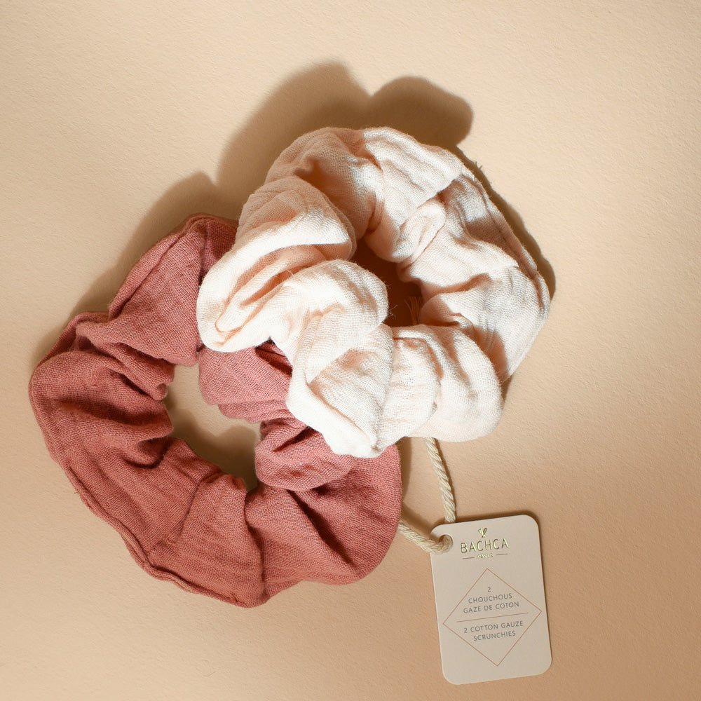 Duo de chouchous Bachca en gaze de coton, un rose poudré et un vieux rose, accompagnés de leur étiquette, photographiés sur une surface beige.