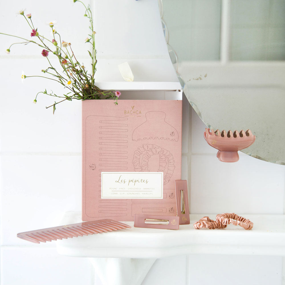 Coffret Les Pépites Bachca en bois de rose posé dans une salle de bain, contenant peigne, pinces, chouchous et barrettes assortis, accessoires cheveux élégants.