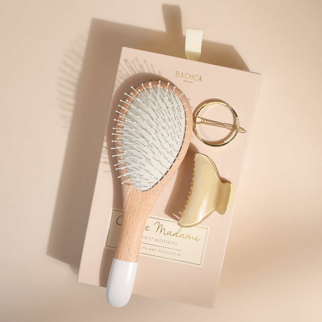 Coffret Madame Bachca avec brosse à cheveux en bois, pince crème et barrette ronde dorée, posé sur un fond beige doux.