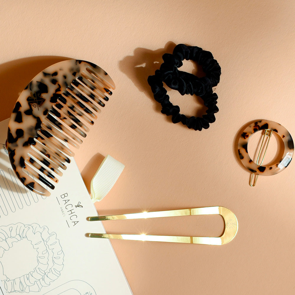 Coffret Les Pépites écaille Bachca comprenant un peigne demi-lune en acétate, une pince circulaire écaille, une épingle dorée et deux chouchous noirs, disposés sur fond beige.