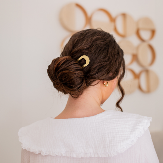Chignon bas élégant maintenu par un pic doré signé Bachca, dans une ambiance douce et naturelle.
