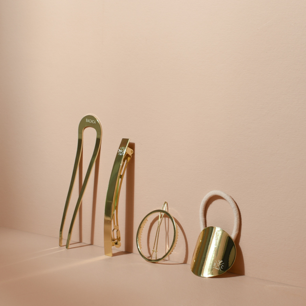 Accessoires cheveux dorés de la marque Bachca posés sur un fond studio rose pâle.