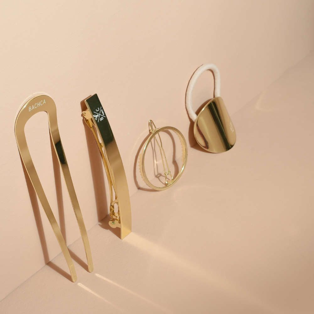 Quarte accessoires cheveux dorés posés sur un mur avec un fond studio rose pâle.