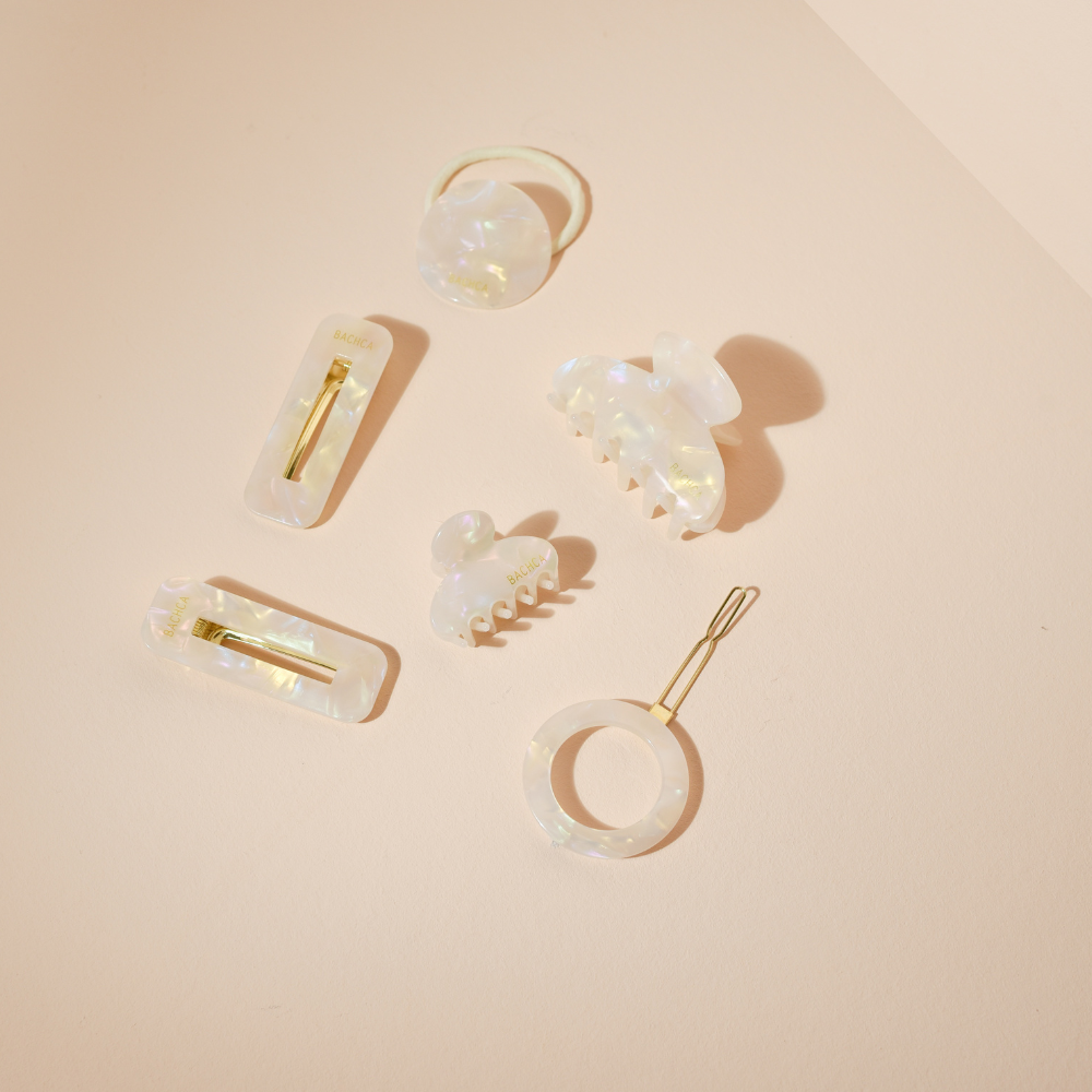 Accessoires cheveux de la marque Bachca. Collection nacre avec pinces et barrettes posées sur un fond studio rose pâle.
