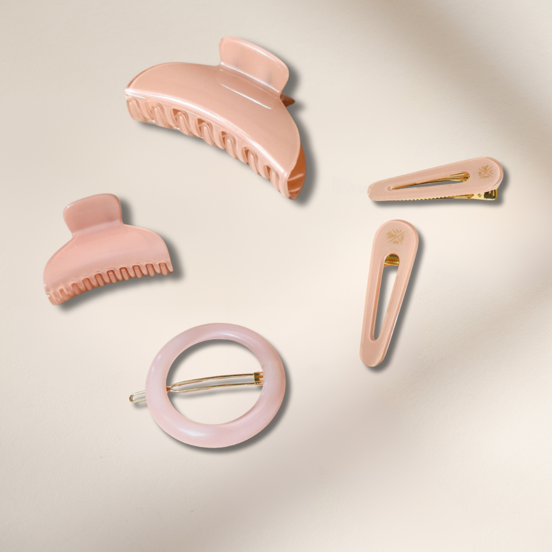 Accessoires cheveux rose dragée, pinces et barrettes réunis sur un fond studio rose pâle.