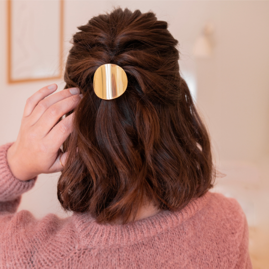 Cheveux bruns mi-longs attachés en demi-queue avec un élastique à plaque dorée Bachca, coiffure chic et naturelle.