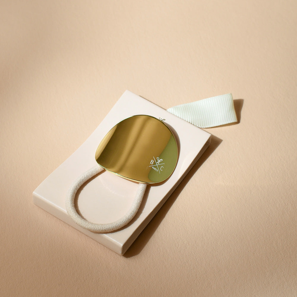 Élastique cheveux Bachca avec plaque ronde dorée, présenté sur son packaging élégant, accessoire raffiné pour sublimer vos coiffures.
